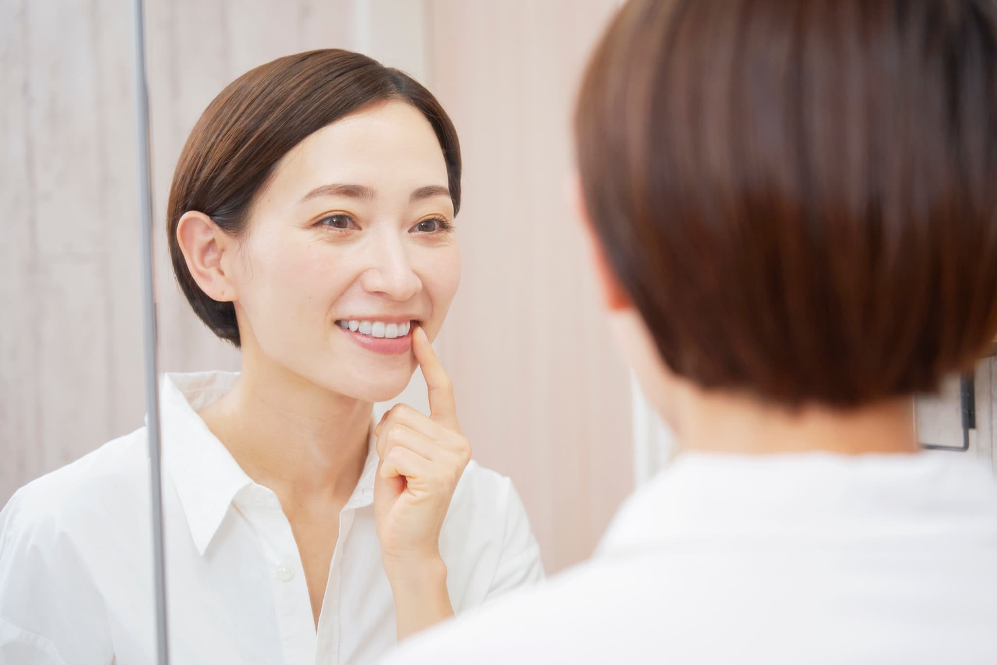 セラミックの歯を指さし鏡を見る女性