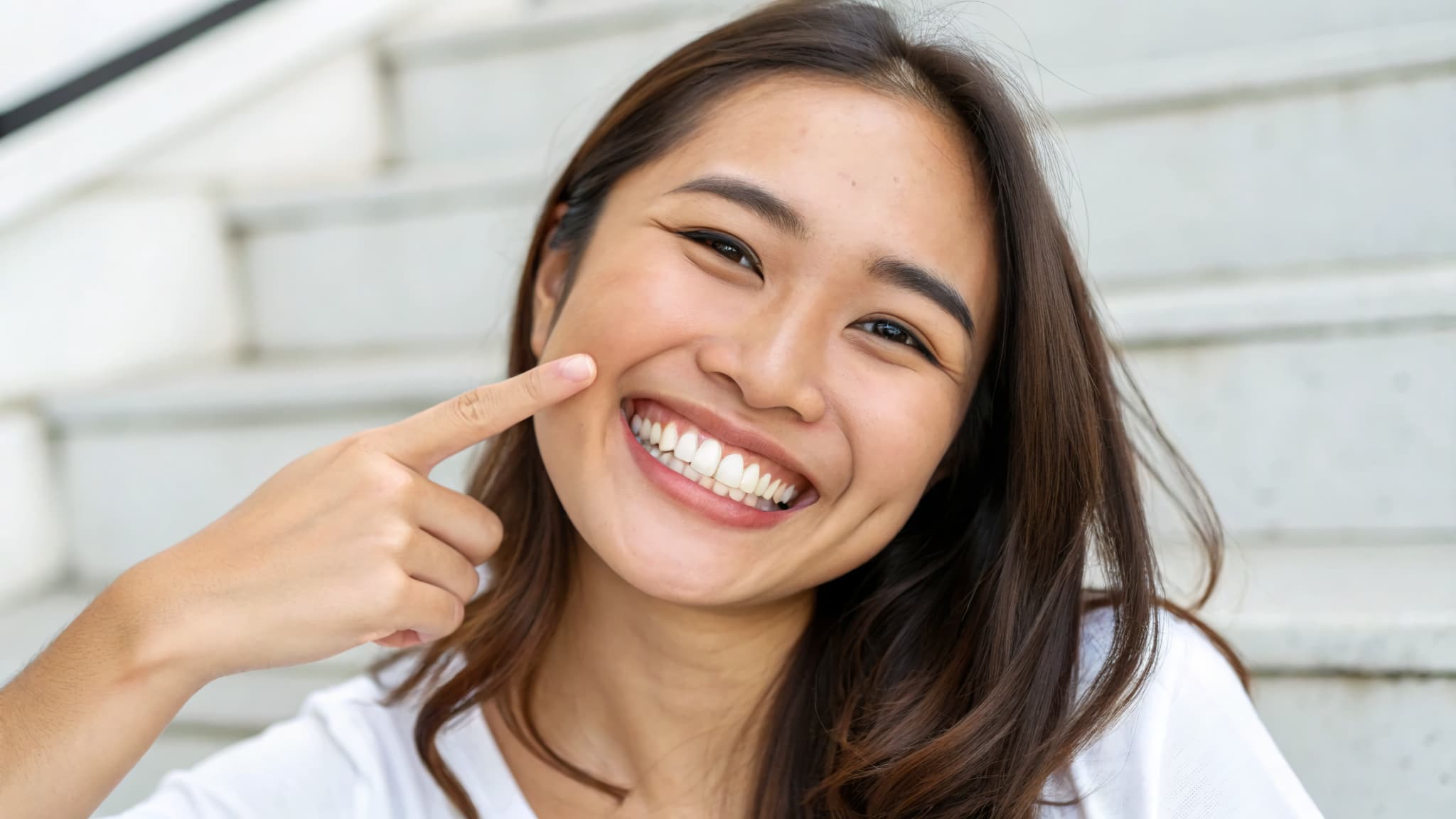 笑顔で歯を指さす親知らずが生えてきた女性