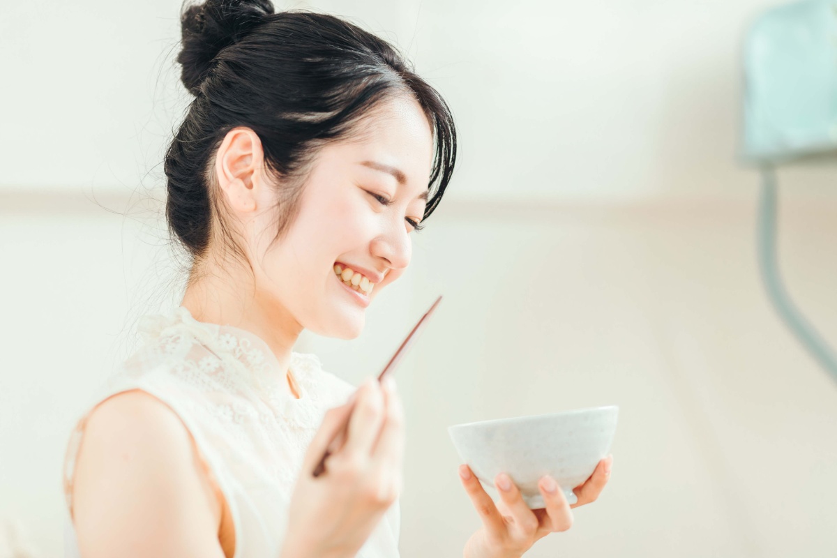 お茶碗と箸を持って笑顔で食事をする女性